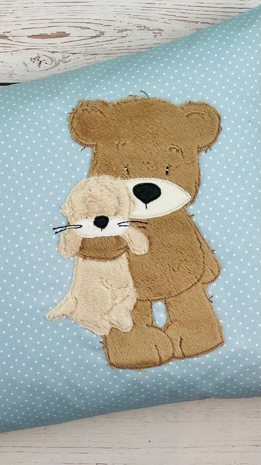 Kuschelkissen bestickt mit Teddybär der einen kleinen Otter im Arm hält. Personalisierbar mit Name und Geburtsdatum.