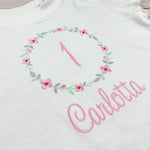 Geburtstagsshirt bestickt mit Blumenkranz und Name. Blumenkranz in den Farben mint, grau und rosa gehalten. Schrift und Zahl in rosa.