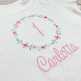 Geburtstagsshirt bestickt mit Blumenkranz und Name. Blumenkranz in den Farben mint, grau und rosa gehalten. Schrift und Zahl in rosa.