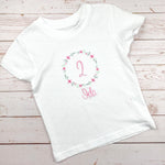 Geburtstagsshirt bestickt mit Blumenkranz und Name. Blumenkranz in den Farben mint, grau und rosa gehalten. Schrift und Zahl in rosa.