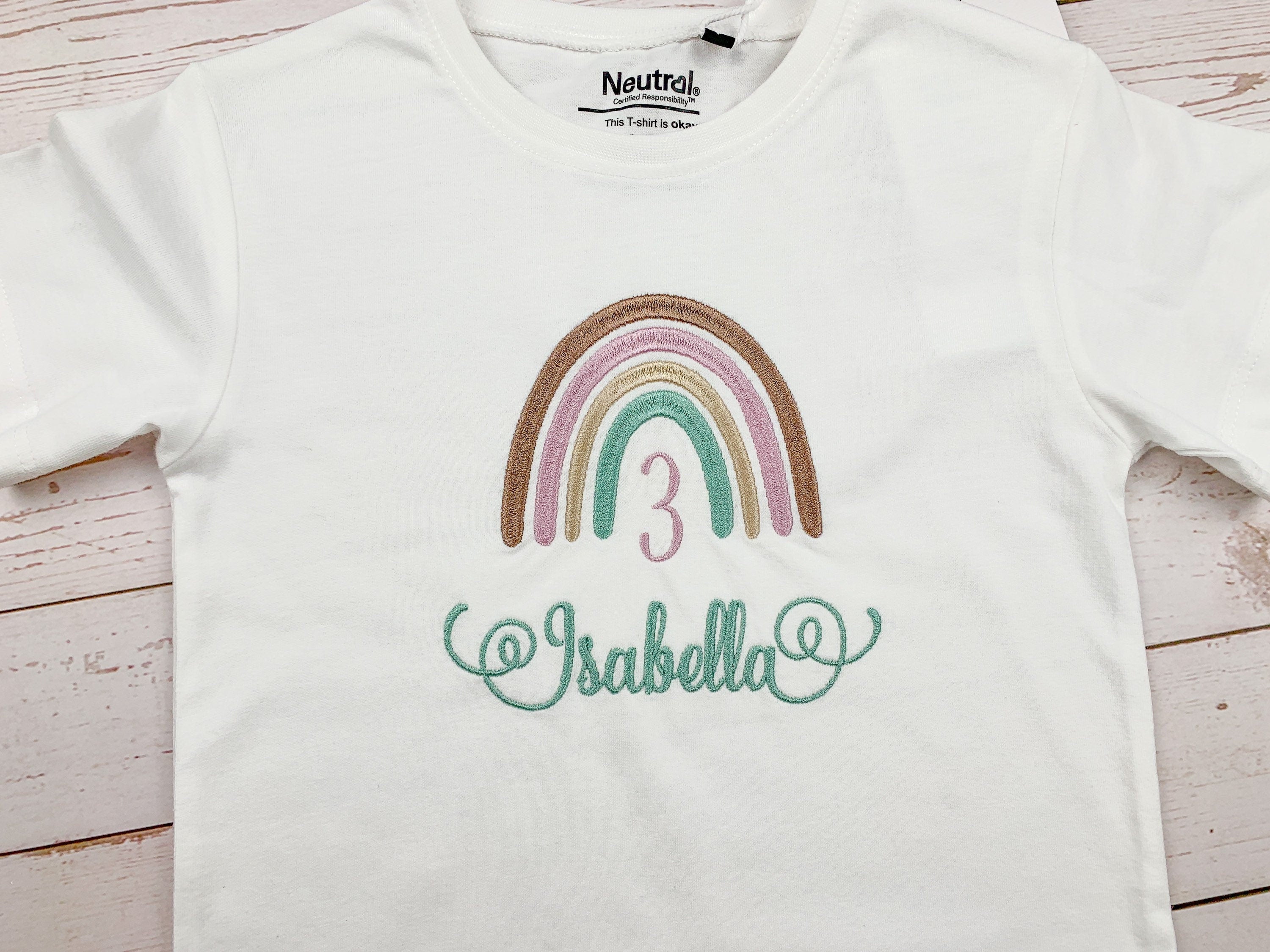 Geburtstagsshirt mit Boho Regenbogen, personalisiert mit Name und Geburtszahl. Farben des Regenbogen - braun, lila, beige, mint. Schrift mit schnörkeln am Anfang und Ende.