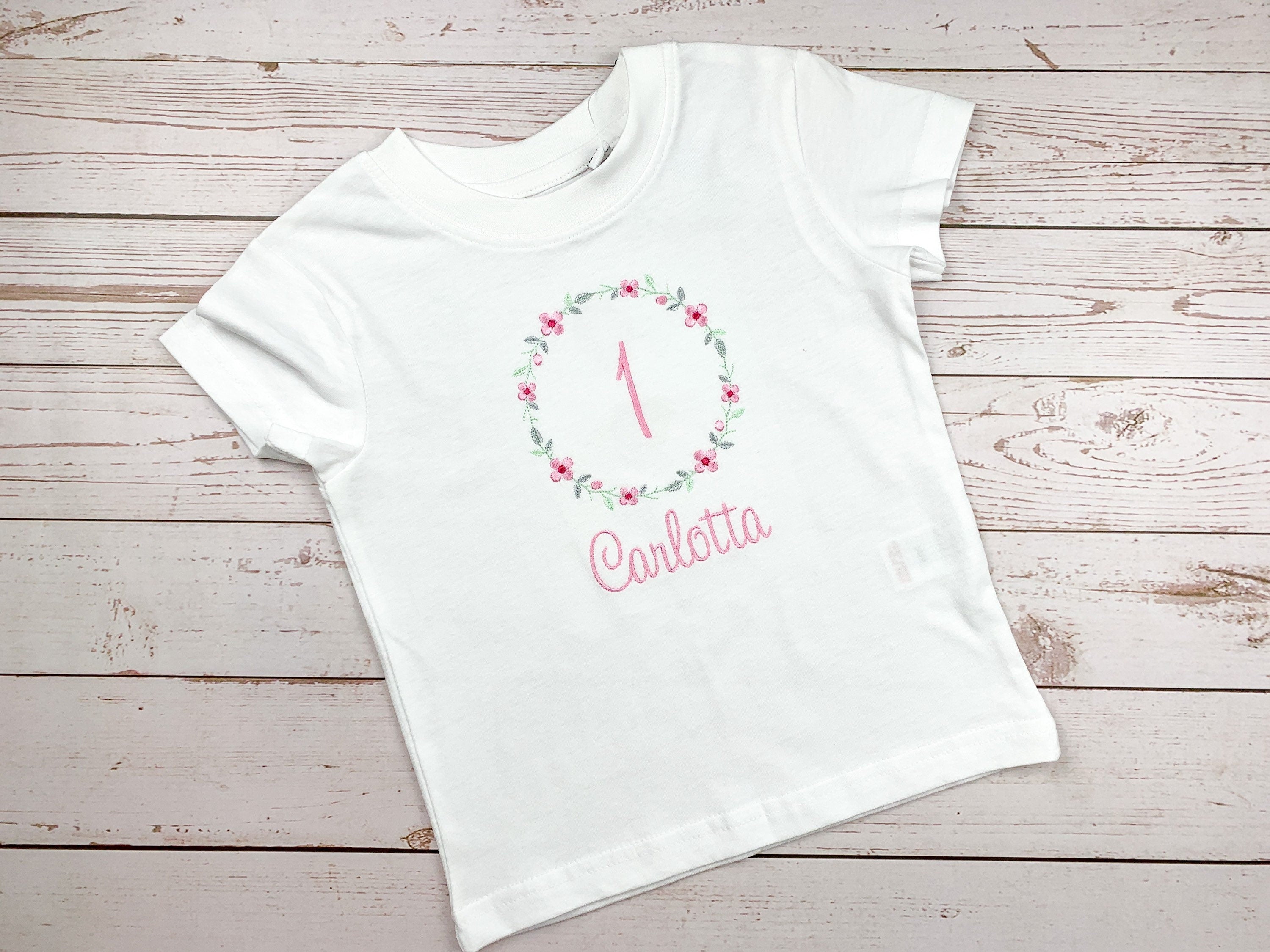 Geburtstagsshirt bestickt mit Blumenkranz und Name. Blumenkranz in den Farben mint, grau und rosa gehalten. Schrift und Zahl in rosa.
