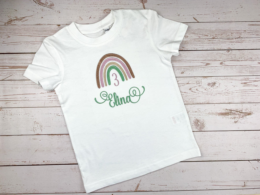 Geburtstagsshirt mit Boho Regenbogen, personalisiert mit Name und Geburtszahl. Farben des Regenbogen - braun, lila, beige, mint. Schrift mit schnörkeln am Anfang und Ende.