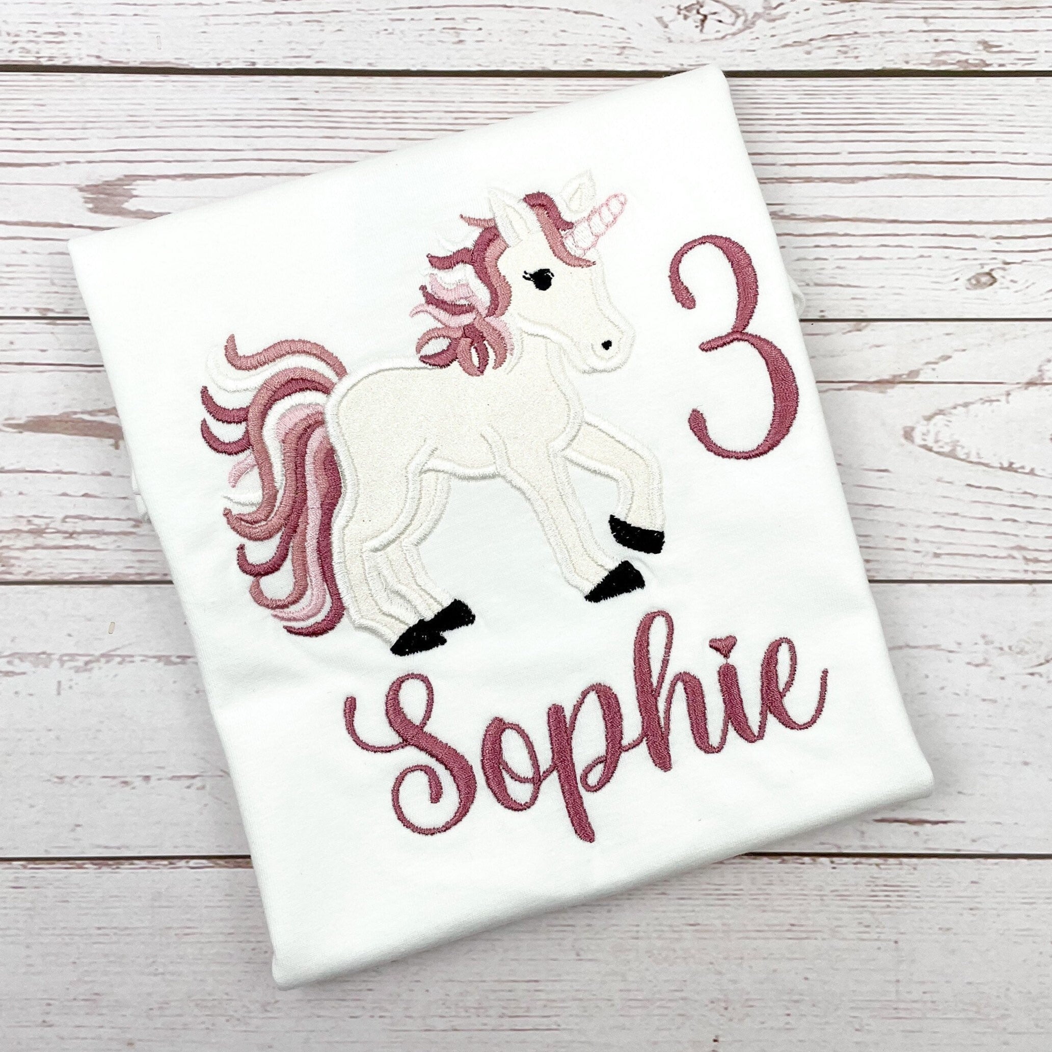 Geburtstagsshirt bestickt mit Glitzer- Einhorn. Das Einhorn ist mit Glitzerstoff unterlegt, Mähne in den Farben weiß rosa und altrosa gehalten.