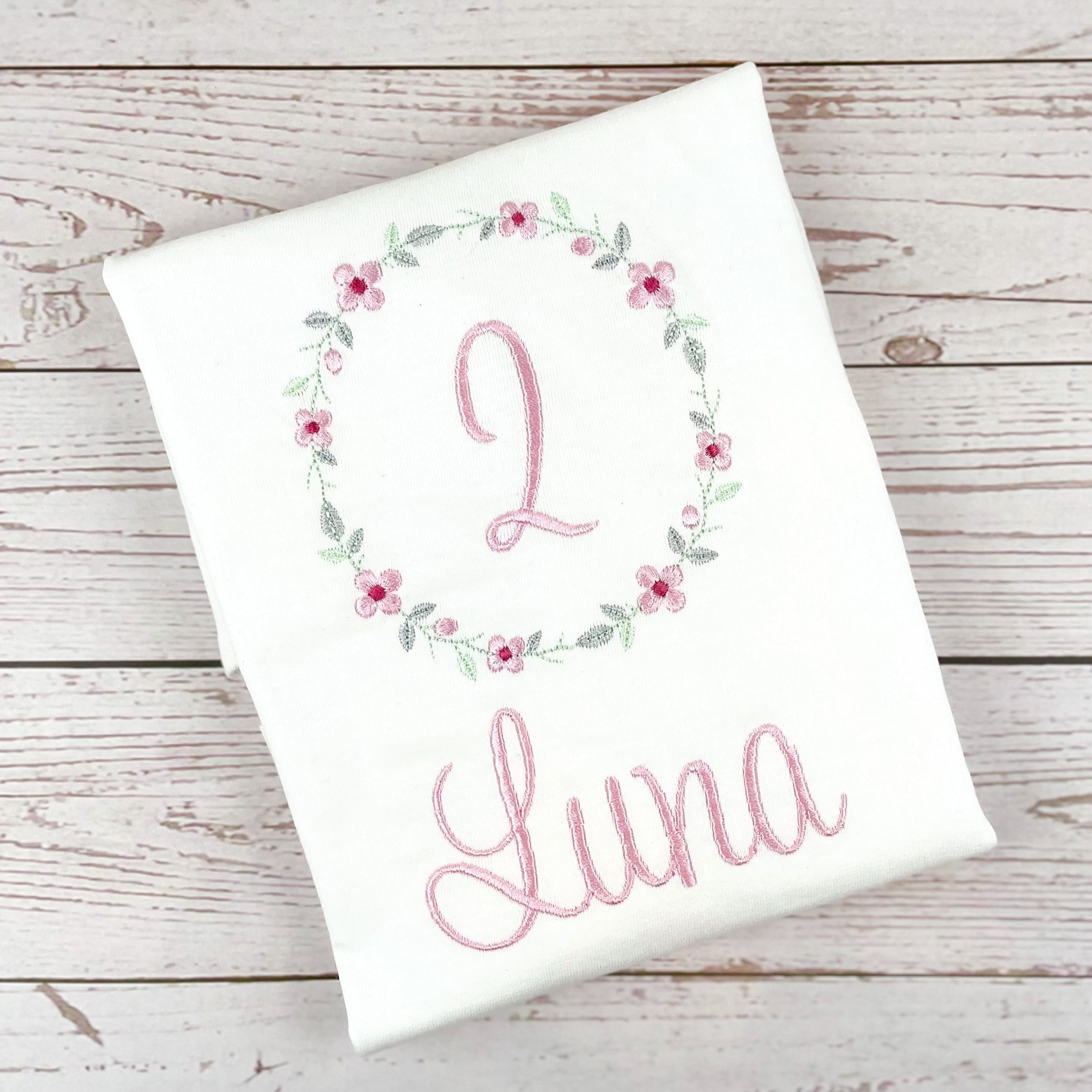 Geburtstagsshirt bestickt mit Blumenkranz und Name. Blumenkranz in den Farben mint, grau und rosa gehalten. Schrift und Zahl in rosa.